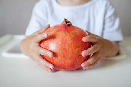 Pomegranate fruit in the hands of a small child close-up. The symbol of the Jewish new year. Rosh Hashana. High quality photoの写真素材