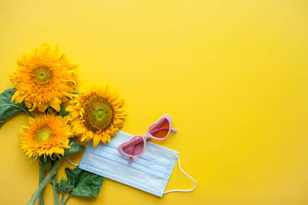 Arrangement of pink heart-shaped sunflower-shaped sunglasses and protective medical mask on bright yellow background. High quality photoの写真素材