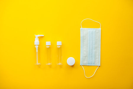 Layout on a bright yellow background. Cosmetic jars and protective medical mask. Travel set. High...