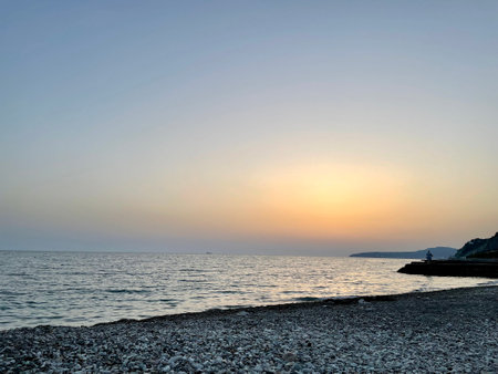 Tranquil sunset over pebble beach with calm waves and distant silhouette. High quality photoの写真素材