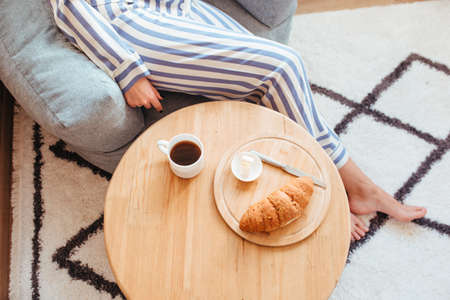 a woman in pajamas in the morning at a table drinks coffee and eats sweets cheesecake sweet macaroni. the concept of breakfast with sweets. top viewの写真素材
