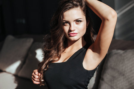 beautiful woman in black dress sits on the sofa and touches her hair.の写真素材