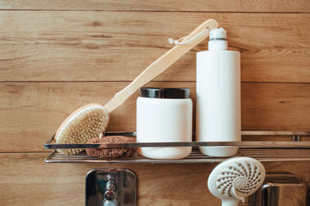 A bath sponge, a body massager brush, a penza, a bottle of shampoo and hair balm is on a shelf in a bathroom with a wooden wall. bath and shower conceptの写真素材