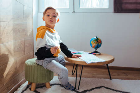 a fair-haired boy is drawing. to get ready for school .there is a globe on the tableの写真素材