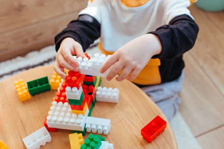 a blond boy is playing with a construction kit, with a wooden wall in the background. close-upの写真素材