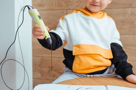 a blonde boy draws with a 3D pen .on the back wall is a wooden backgroundの写真素材