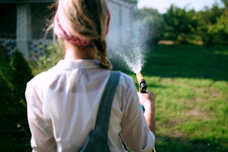 a young woman in a white shirt and denim overalls watering the lawn. gardening concept and landscape designの写真素材