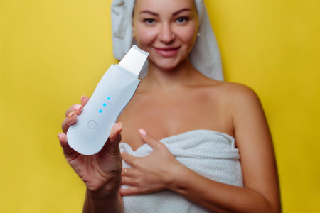 Ultrasonic scrubber for facial skin cleansing. Girl in the bathroom takes care of her face