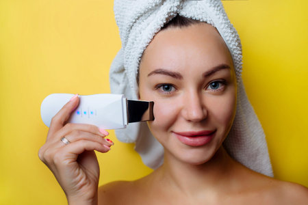 Ultrasonic scrubber for facial skin cleansing. Girl in the bathroom takes care of her face