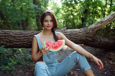 Picnic in nature and healthy eating. A sexy girl in the woods eats watermelon. Portrait of a woman with a berry in her handsの写真素材