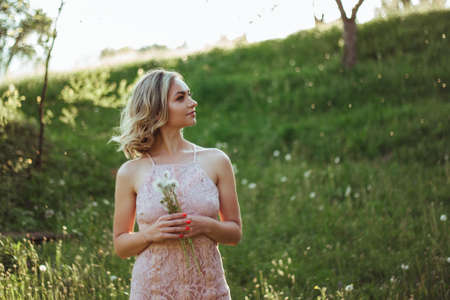 a woman at sunset in a field of dandelions in a pink dress . the concept is not allergicの写真素材