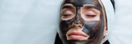 banner . cosmetologist applying black mask on pretty woman face wearing black gloves, gorgeous woman...