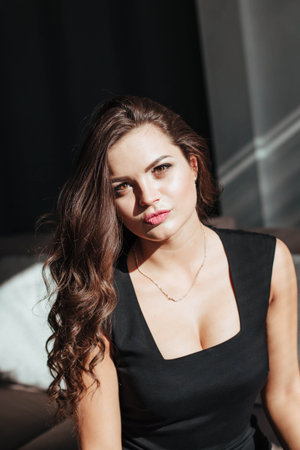 Portrait of a sexy brunette in a black dress on a dark background. girl takes off her dress slowly...