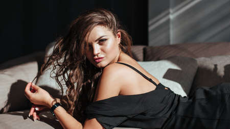 Portrait of a sexy brunette in a black dress on a dark background. girl takes off her dress slowly in the bedroomの写真素材