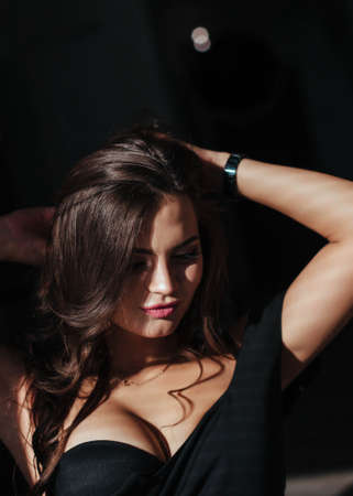Portrait of a sexy brunette in a black dress on a dark background. girl takes off her dress slowly in the bedroomの写真素材