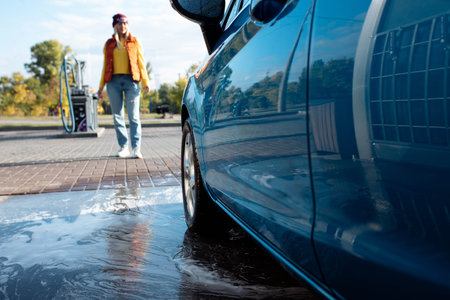 portrait young, smiling, happy, attractive woman washing automobile at manual car washing self service station, cleaning with foam, pressured water. Transportation, auto, vehicle care conceptの写真素材