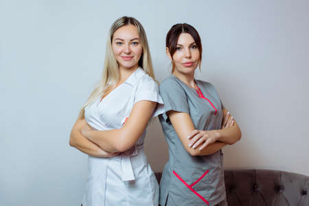 Two young beautiful sexy women cosmetologists colleagues in white stylish clothing standing and smiling.の写真素材
