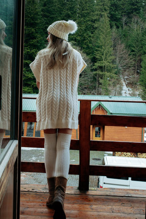 A sexy girl in a white sweater and stockings on the balcony admires the beauty of nature. wool...