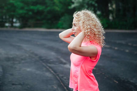 A young curly blonde of athletic build performs a warm-up before training at the stadium. Outdoor sportsの写真素材