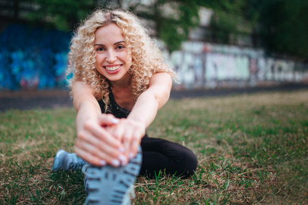 A young curly blonde of athletic build performs a warm-up before training at the stadium. Outdoor sportsの写真素材