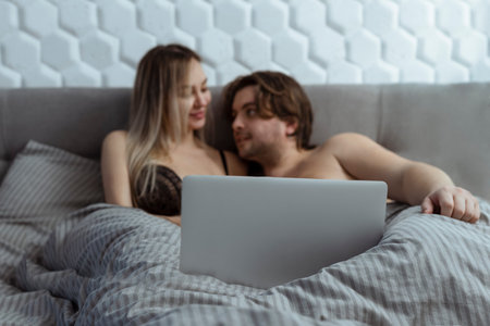 Couple watching porn movie over laptop in bedroomの写真素材