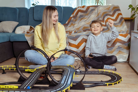 Mom and little son play racing on the carpet at home, have fun and hug. Single mother raises her son...