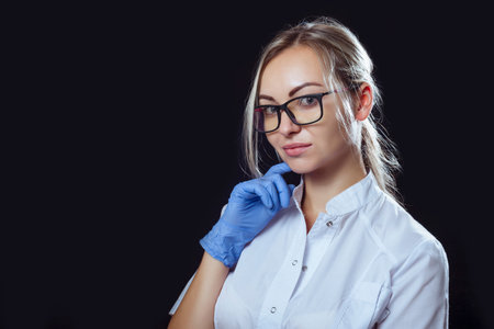 Portrait of a girl doctor on a black background in glasses for vision and glovesの写真素材