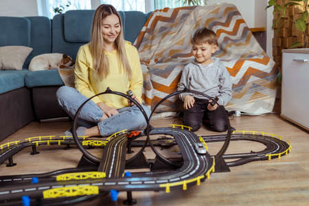 Mom and little son play racing on the carpet at home, have fun and hug. Single mother raises her son by playing carsの写真素材