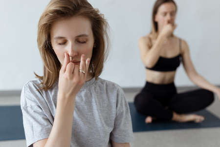 Two athletic attractive girls sit in lotus position on yoga mat indoors .Yoga, fitness and healthy lifestyleの写真素材