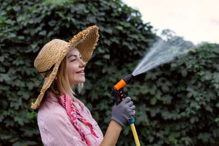 portrait of happy young woman gardener watering garden with hose. Hobby conceptの写真素材