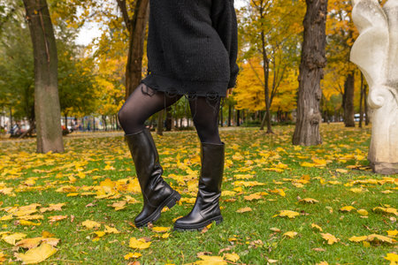 A girl in warm boots poses against a background of fallen foliageの写真素材