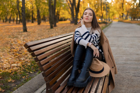 beautiful smiling woman in stylish outfit sitting at the table in a hat and sweater, romantic happy mood, waiting for a boyfriend on a date in a cafe, spring-summer fashion trend, drinking coffeeの写真素材