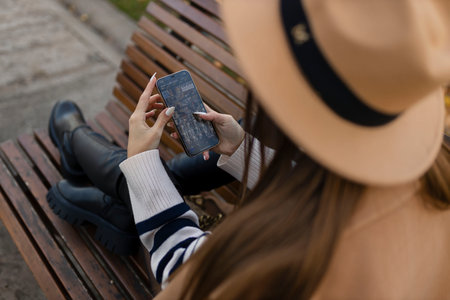 Attractive cheerful brunette girl in trench coat with coffee to go happily using cellphone outdoorの写真素材