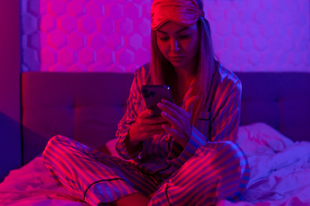 Using mobile phone in glowing neon light. Creative bright color ultraviolet red and blue. Womans hands typing a message on a mobile phoneの写真素材