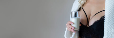 sexy young woman in black lingerie pouring milk on body isolated on greyの写真素材
