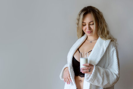 sexy young woman in black lingerie pouring milk on body isolated on greyの写真素材