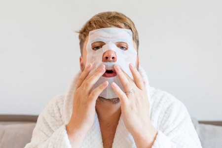 Funny man having fun at home using the face mask for better mood feeling awesome. Portrait of guy doing cosmetic procedures. People skin care conceptの写真素材