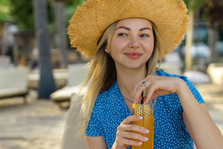 Fashion young woman drinking cocktail in beach bar. Cheerful attractive blonde woman in a dress smiles and drinks a cocktail outdoors. Happy woman enjoying summer time at the beachの写真素材