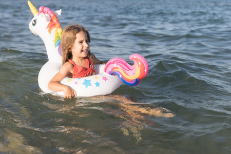 Happy baby girl swimming on an inflatable swimming unicorn in the seaの写真素材