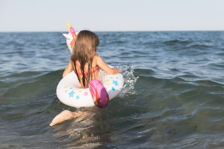 Happy baby girl swimming on an inflatable swimming unicorn in the seaの写真素材