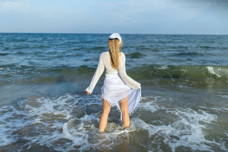 Beautiful girl in the sea. The woman enters the sea. Blue ocean. Girl in a white cape. Beautiful...