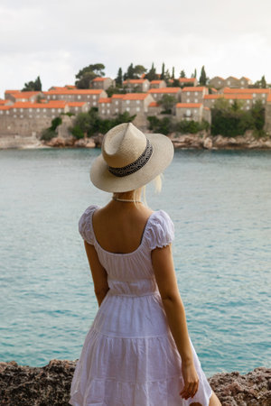 girl tourist in a hat looks from a top on the island of Sveti Stefan in Montenegro and the seaの写真素材