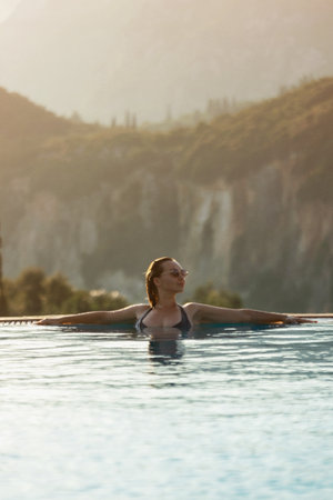 Slim woman in swimsuit walking by the edge of infinity pool with jungle viewの写真素材
