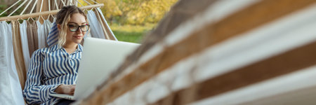 Young woman lies in a hammock with a laptop in glasses outside at homeの写真素材