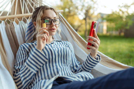 A beautiful girl in a hammock uses a smartphone outdoor