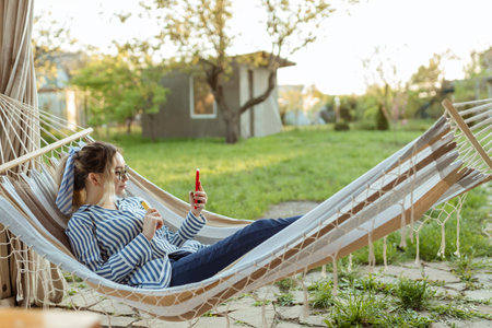 A beautiful girl in a hammock uses a smartphone outdoorの写真素材