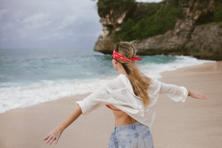 young attractive happy woman dancing twirling on seashore sunny summer fashion style in white shirt...