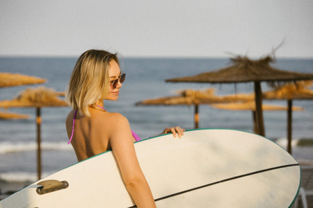 Attractive young woman in sunglasses and bikini holding a surfboard on a sunny beach. Summer...