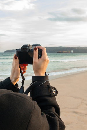 Hands holding a digital camera while photographing seascape on sandy beach, capturing outdoor moments with modern photography equipment and natural coastal scenery.の写真素材