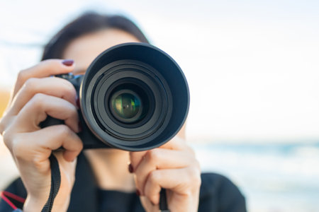 Low-angle view of a female photographer holding a professional camera against the blue sky, capturing outdoor moments and focusing on creative photography.の写真素材